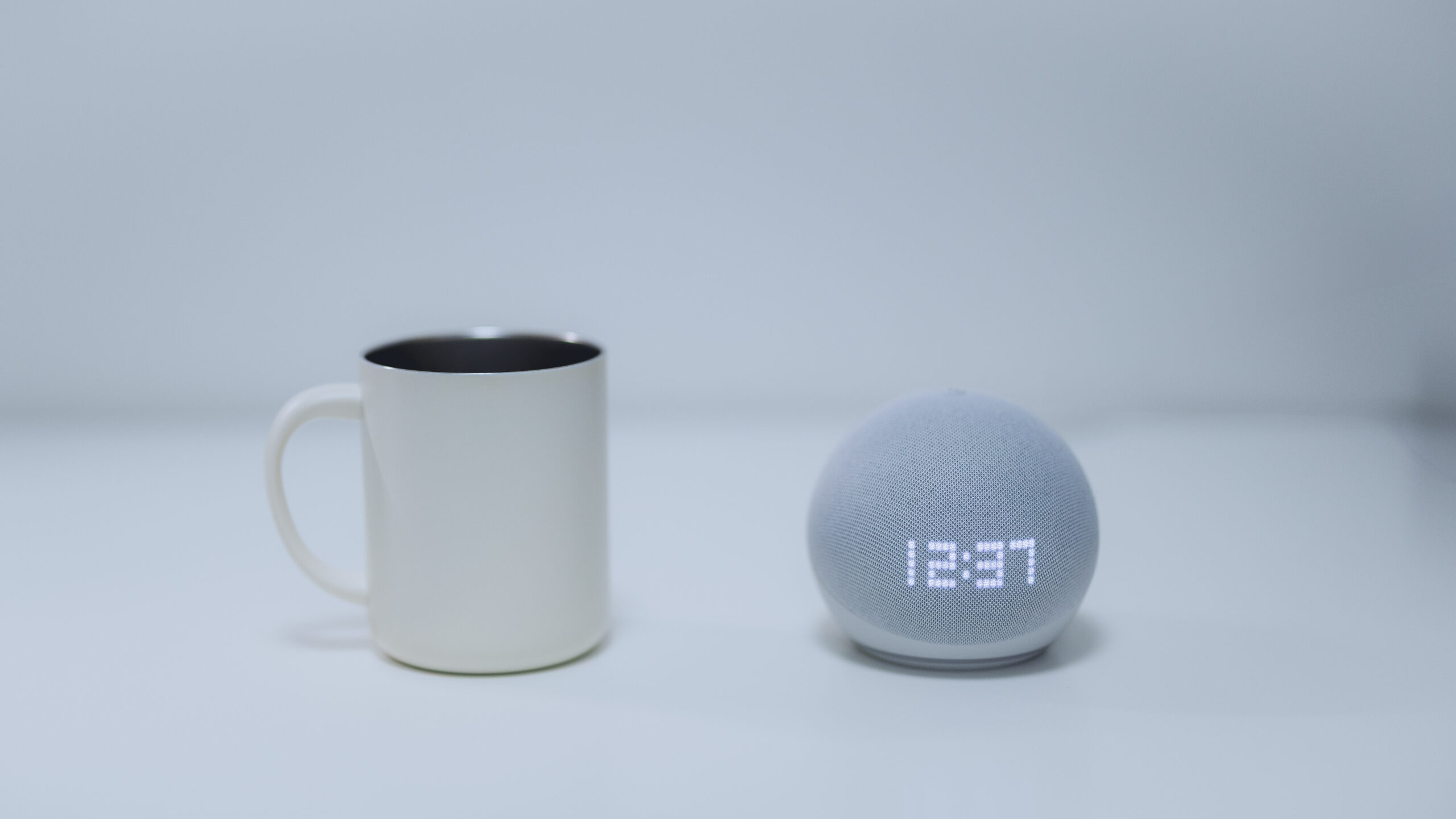 マグカップと並べて置かれた、コンパクトなスマートスピーカー（Amazon Echo Dot）。その小ささで置き場所を選ばないことを示している。